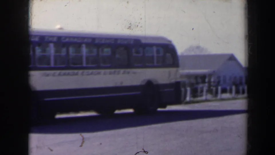 The bus remains parked on the roadside, with Canada Coach Lines lettering visible and a small white building behind it.