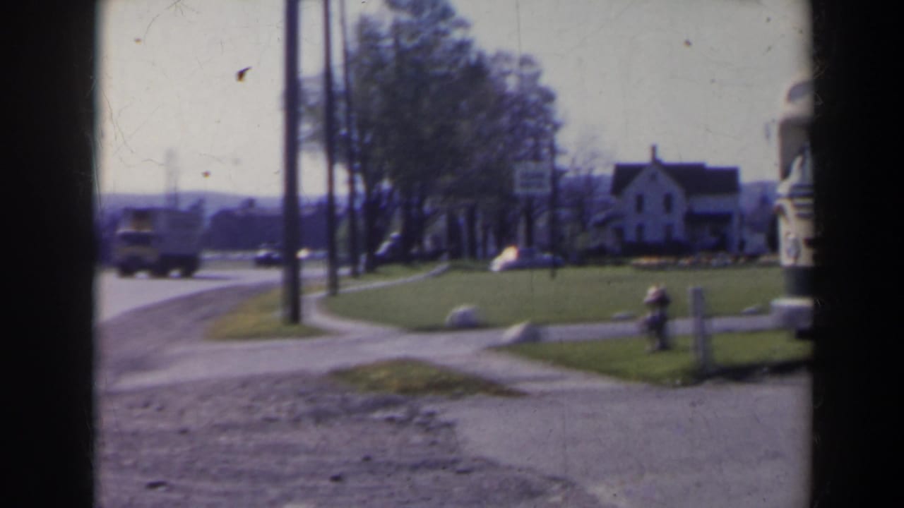 1963 8mm view near Niagara Falls, Canada, showing a quiet road, distant truck, white house, hydrant, grass verge, and utility poles.