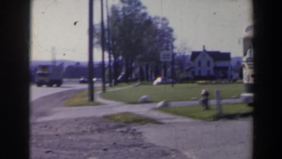 1963 8mm view near Niagara Falls, Canada, showing a quiet road, distant truck, white house, hydrant, grass verge, and utility poles.