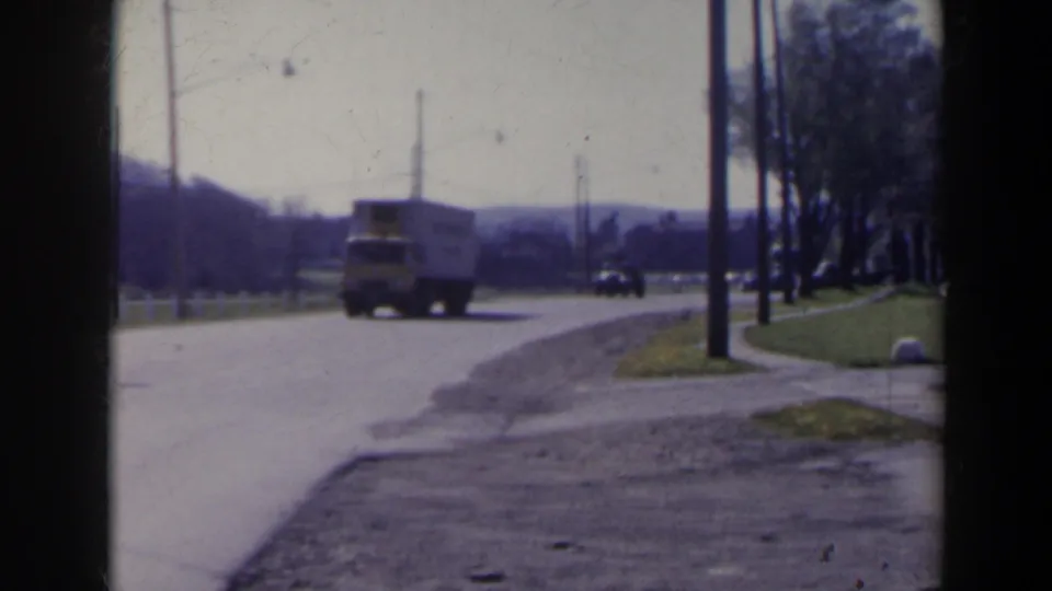 1963 8mm roadside view near Niagara Falls, Canada, with a yellow-and-white truck approaching on a paved road under bright daylight.
