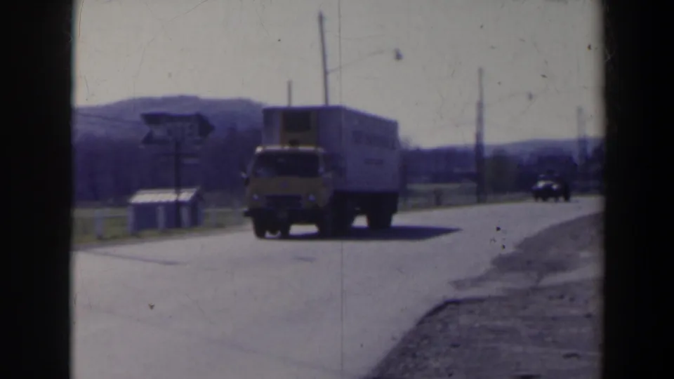 1963 8mm frame near Niagara Falls, Canada, showing the truck close to camera on a road with a motel sign and utility poles nearby.