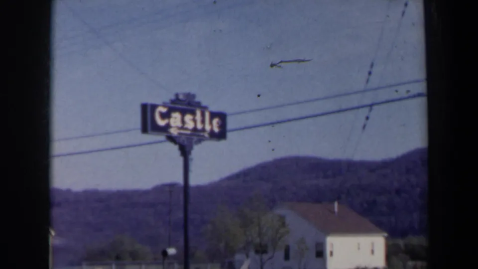 Final 1963 Niagara Falls, Canada frame showing the Castle sign, overhead wires, wooded hills, white building, trees, mailbox, and dark film edge.