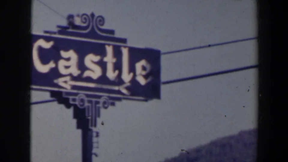 Close 1963 Niagara Falls frame of the blue Castle sign with decorative lettering, arrows, support post, and wires crossing the sky.