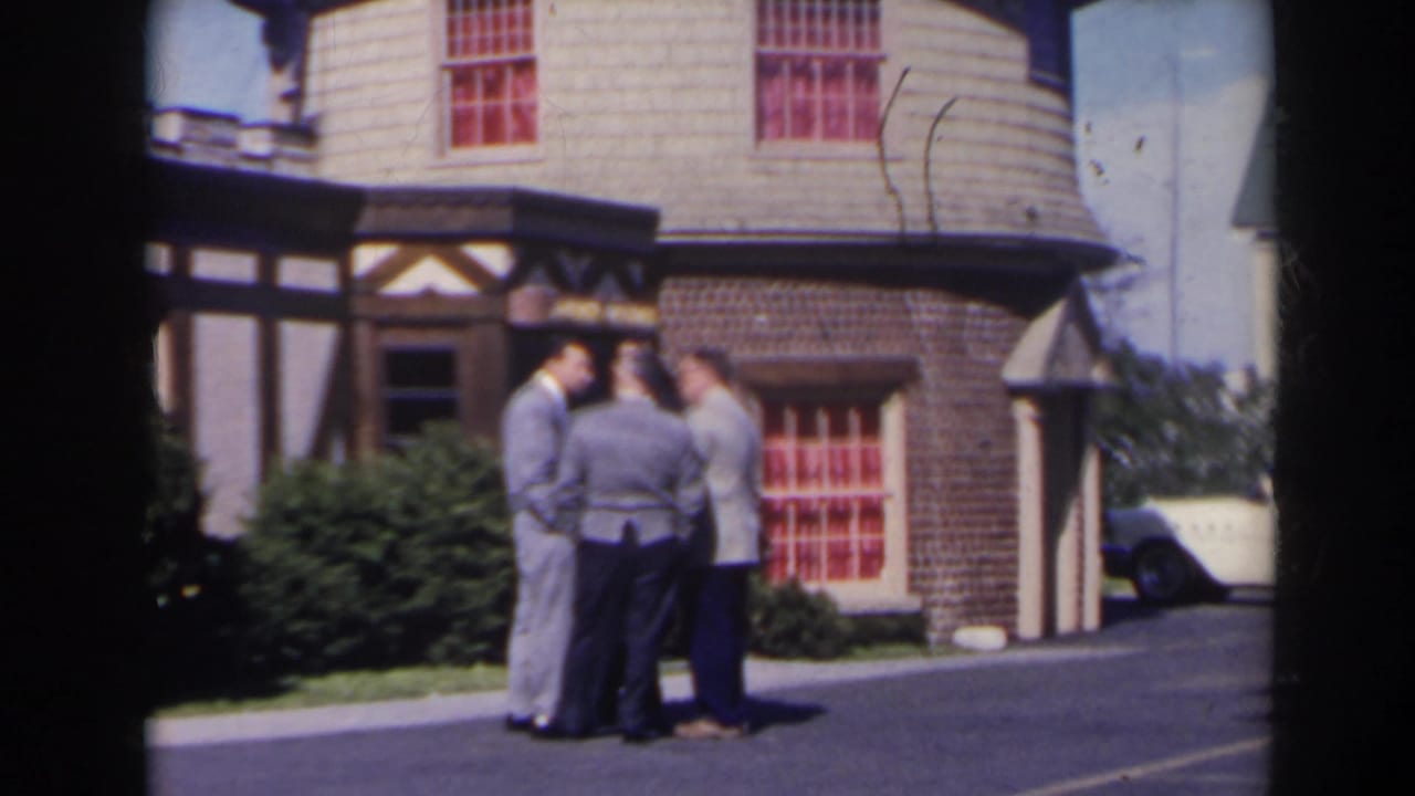 Three adult men converse outside a Tudor-style building in likely 1963 Niagara Falls, Canada home-movie footage.