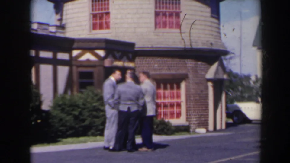 Three adult men converse outside a Tudor-style building in likely 1963 Niagara Falls, Canada home-movie footage.