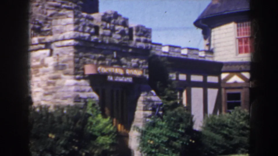 A closer view shows stone castle-like walls, Tudor-style trim, shrubs, and a partly readable cocktail lounge sign.