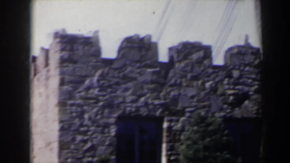 1963 Niagara Falls, Canada frame showing rough crenelated stonework, a dark lower opening, and foliage near the base.