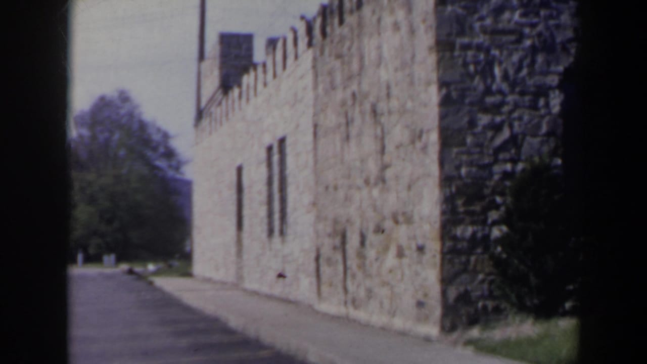1963 Niagara Falls Canada home-movie frame showing a tan stone, castle-like building along a paved walkway in daylight.