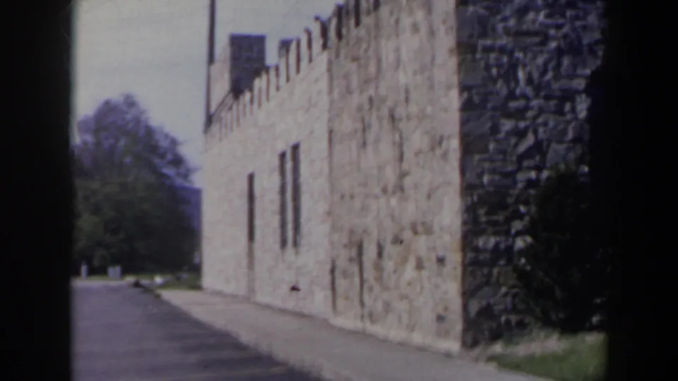 1963 Niagara Falls Canada home-movie frame showing a tan stone, castle-like building along a paved walkway in daylight.