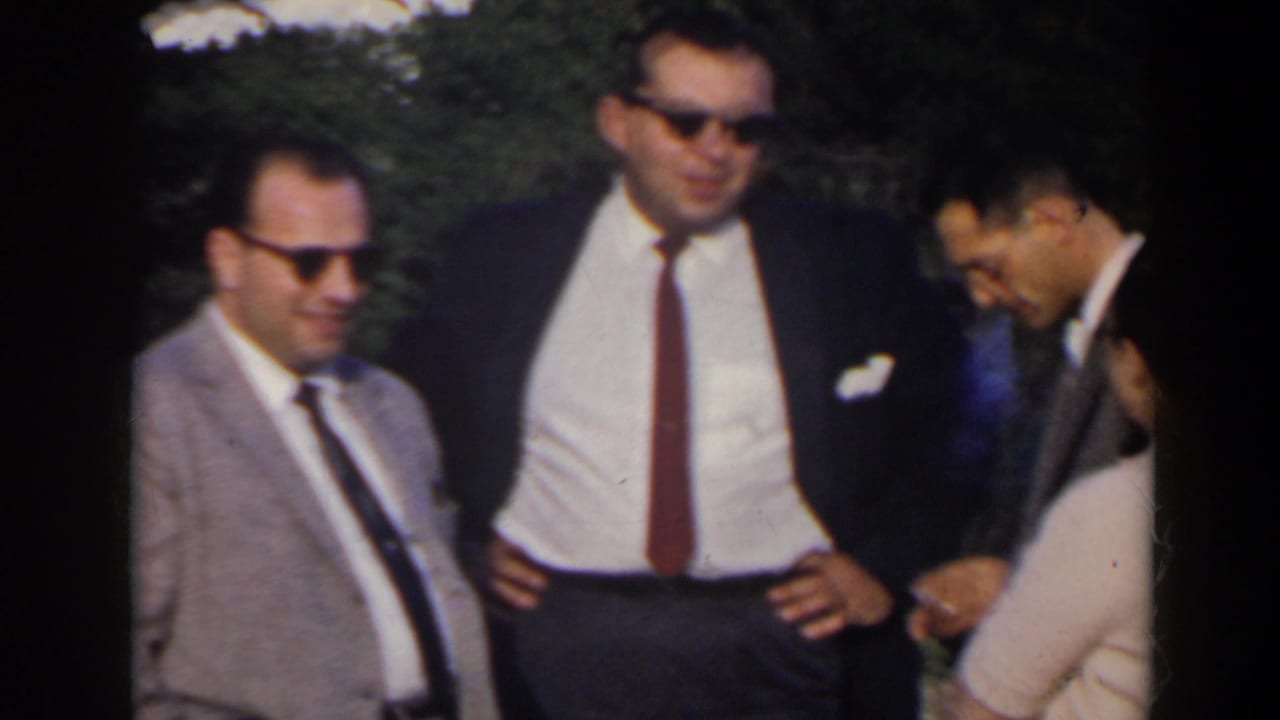 Three adult men in suits and sunglasses stand outdoors in bright daylight.