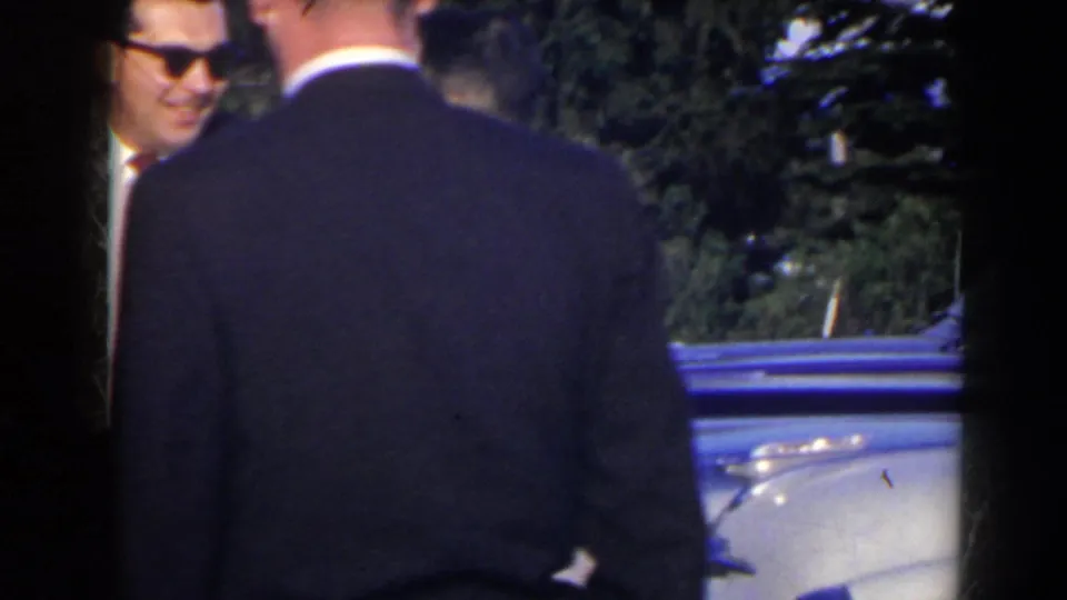 Adult men in suits stand near a light-colored car in a sunlit 1963 Niagara Falls Canada home-movie scene.