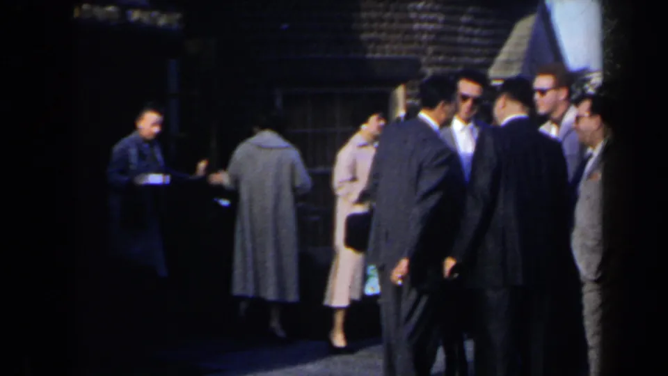 Adults in suits and coats stand near a building entrance in 1963 Niagara Falls home-movie footage.