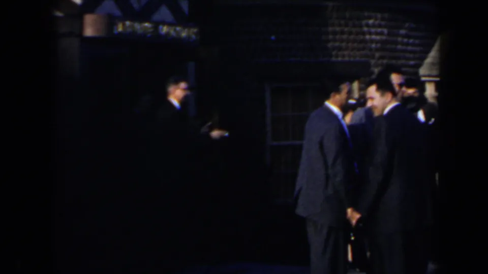 Men in dark suits stand in conversation outside a building in 1963 Niagara Falls home-movie footage.