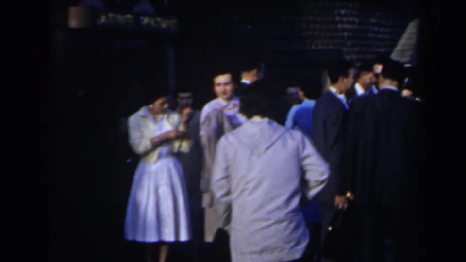 Women in pale dresses and men in suits gather outdoors at night in Niagara Falls, Canada, in a softly focused 1963 8mm frame.