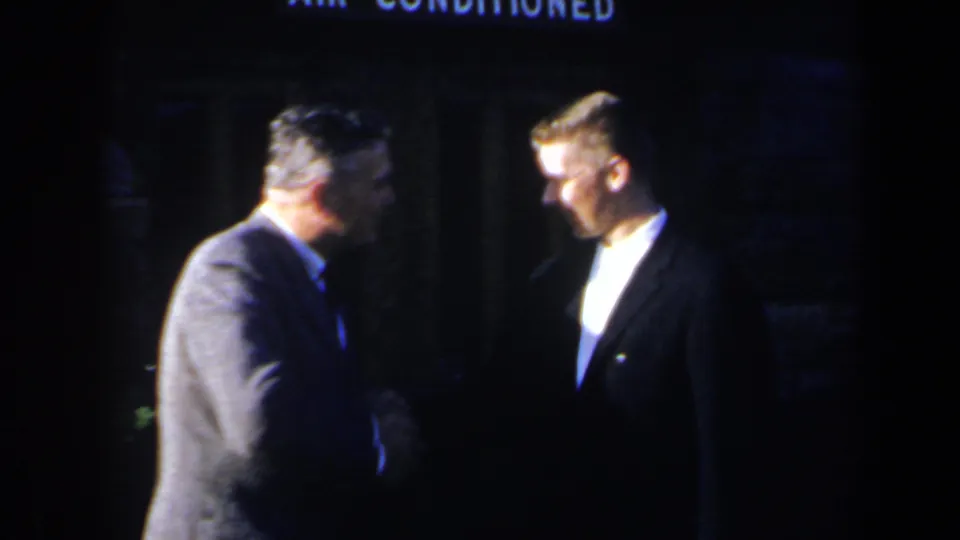 1963 Niagara Falls frame showing two suited men in conversation, apparently shaking hands in a dark outdoor setting.