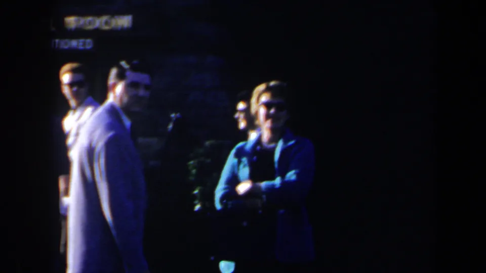 A woman in a blue jacket and sunglasses stands with adults nearby in this 1963 Niagara Falls home-movie frame.