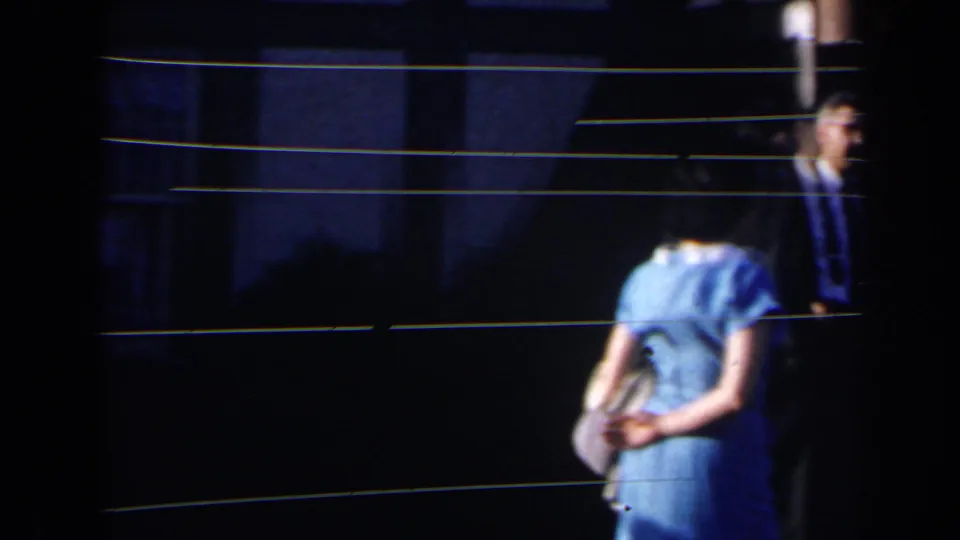 1963 Niagara Falls home-movie frame showing a woman in a light blue dress near a man in a suit at a dim entrance.