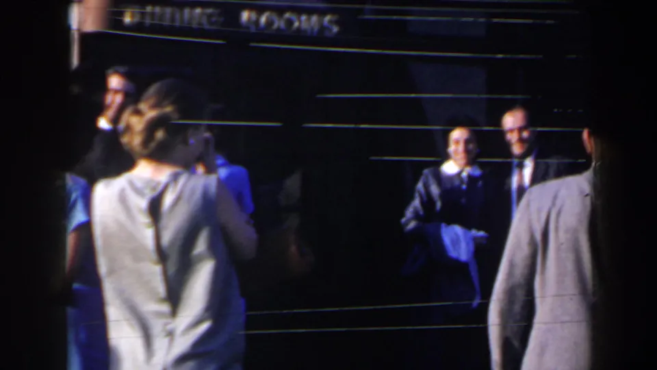 1963 Niagara Falls home-movie frame showing adults in suits and dresses near a dining rooms entrance.