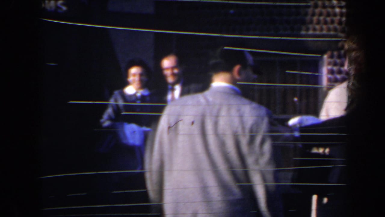 Group of adults near a dark doorway, with a man seen from behind in the foreground.