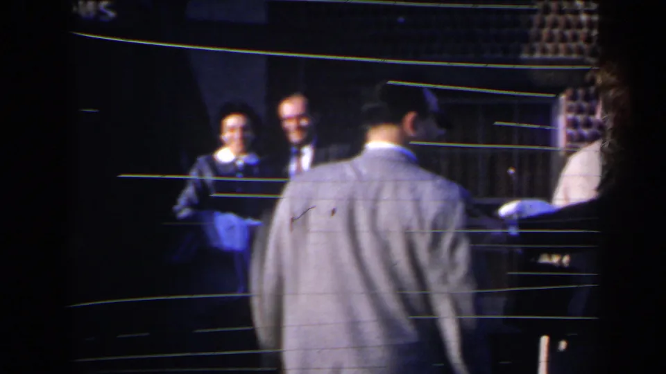 1963 Niagara Falls home-movie frame of guests outside a dining entrance, partly obscured by a foreground figure.