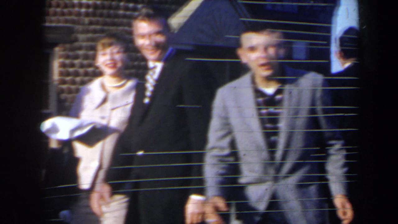1963 home-movie frame from Niagra Falls, Canada showing suited men and a woman in light clothing standing outside in daylight.