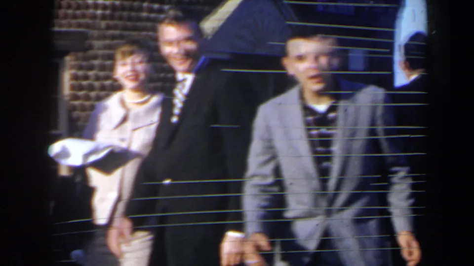 1963 home-movie frame from Niagra Falls, Canada showing suited men and a woman in light clothing standing outside in daylight.