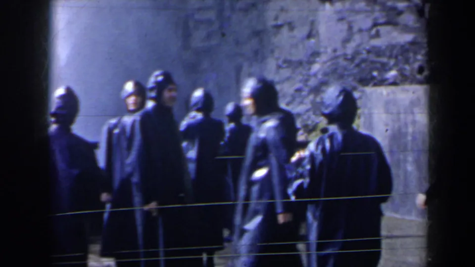 1963 home-movie frame of raincoated Niagara Falls visitors gathered near a rough stone or concrete wall.