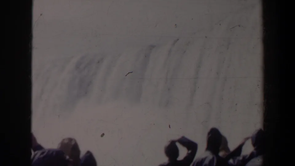 1963 8mm view of Horseshoe Falls with several dark spectator silhouettes at the lower edge against bright spray.