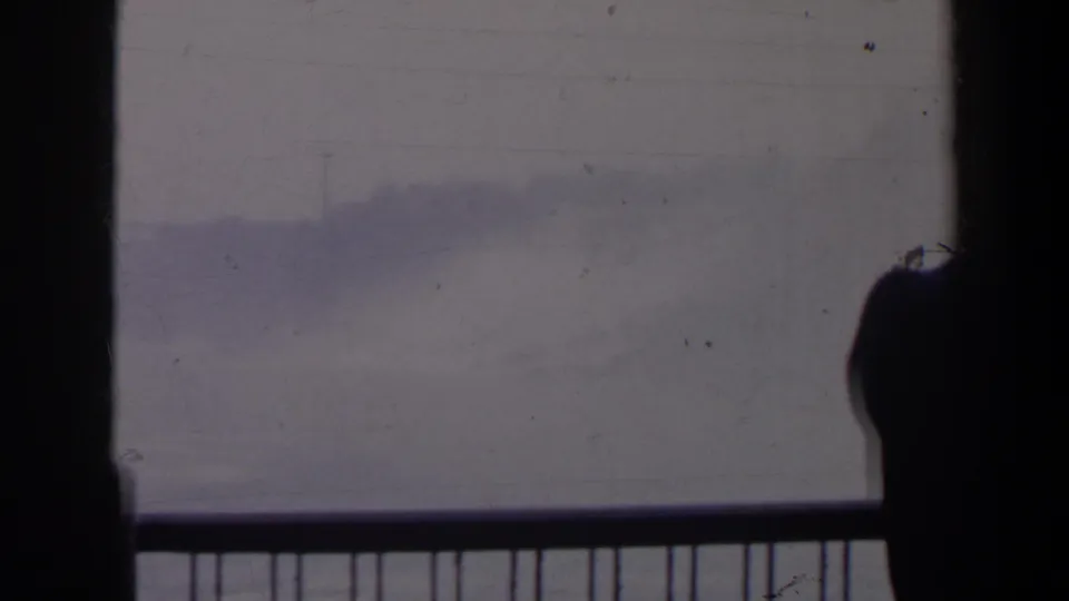 The 1963 home-movie frame holds on a railing and misty Niagara Falls background, with a partially seen visitor silhouette near the lower edge.