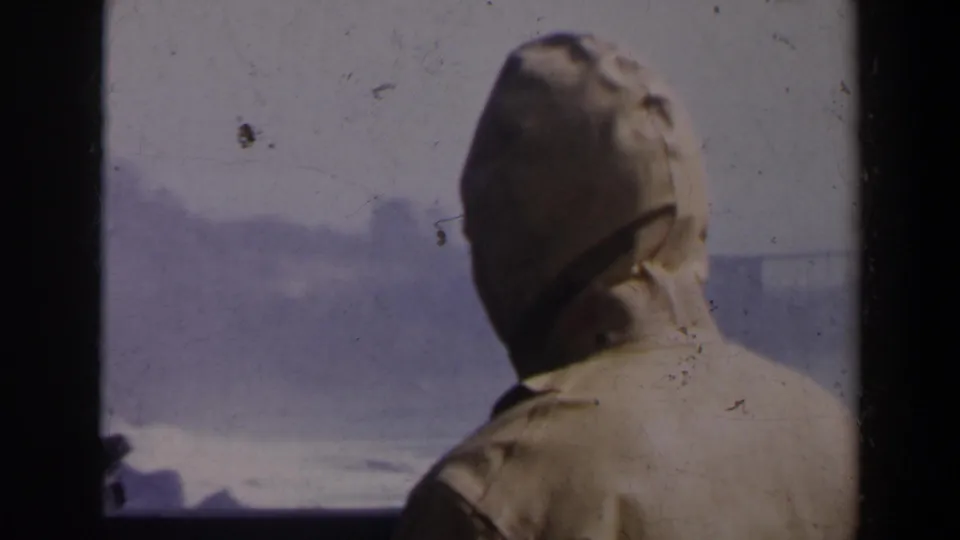 A 1963 home-movie frame shows the back of a light-hooded visitor watching Niagara Falls through haze and spray.