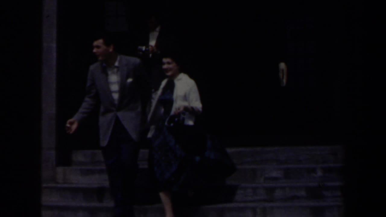 In 1963 Niagara Falls home-movie footage, a couple begins walking hand-in-hand from a grey stone building entrance.