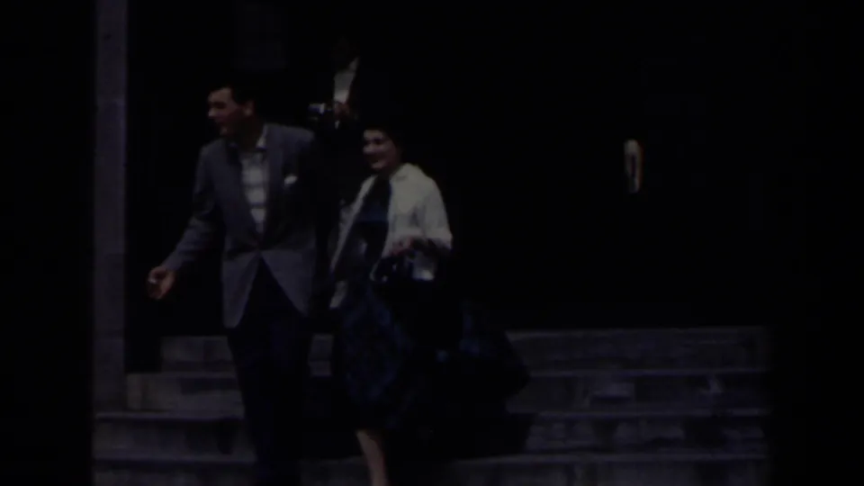 In 1963 Niagara Falls home-movie footage, a couple begins walking hand-in-hand from a grey stone building entrance.