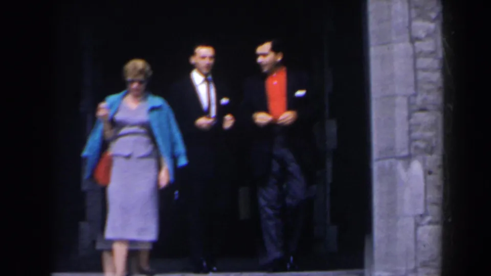 A woman with sunglasses and a red purse walks in front of two men outside the Niagara Falls tunnel entrance.