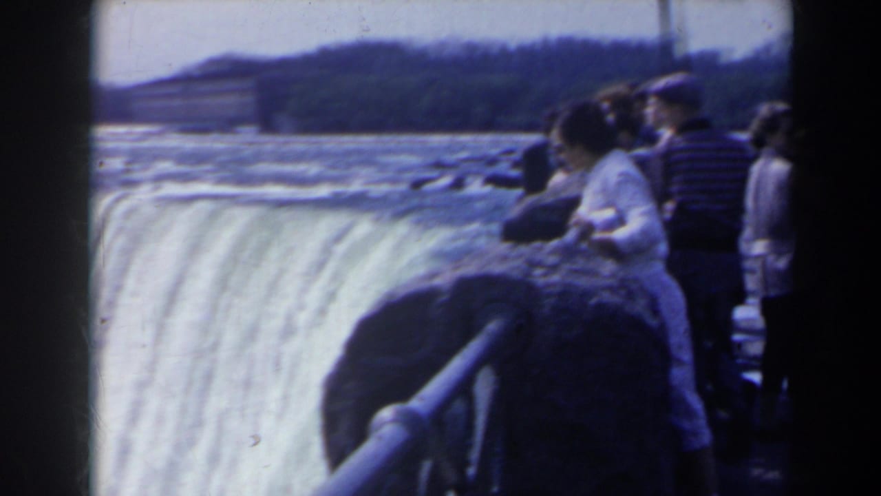 Visitors lean on a stone overlook as the waterfall drops beside them.