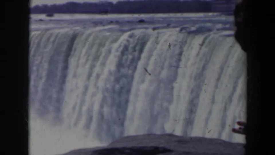 Close home-movie view of Niagara Falls pouring over the edge, with a partial visitor at the right side of the frame.