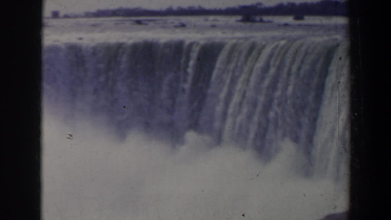 Waterfall crest and mist seen through a soft, blue-tinted 8mm frame.