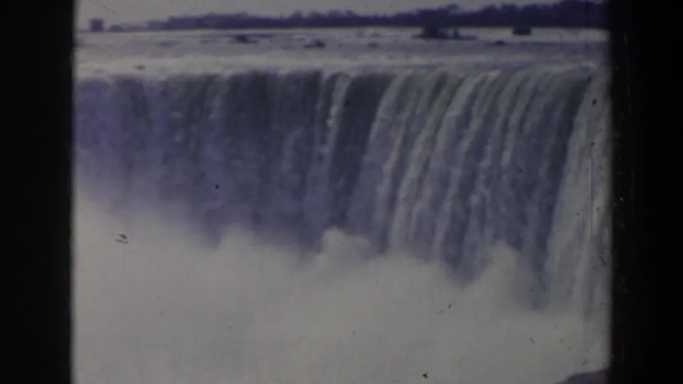 1963 Niagara Falls home-movie frame with water dropping across the upper edge and pale mist obscuring the lower falls.