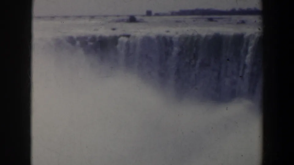 1963 8mm Niagara Falls view with the falls softened by mist, visible film scratches, and a distant horizon line.