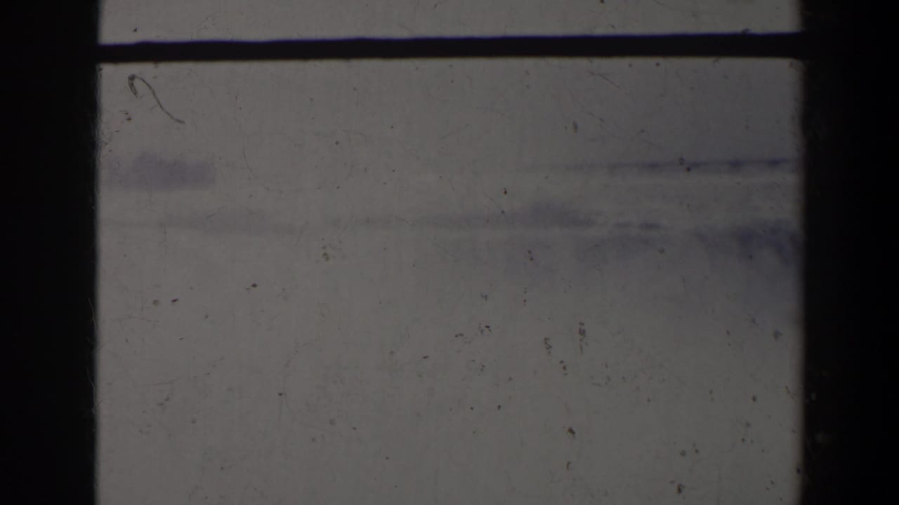 Pale hazy frame with dark vertical film edge and faint distant shapes.