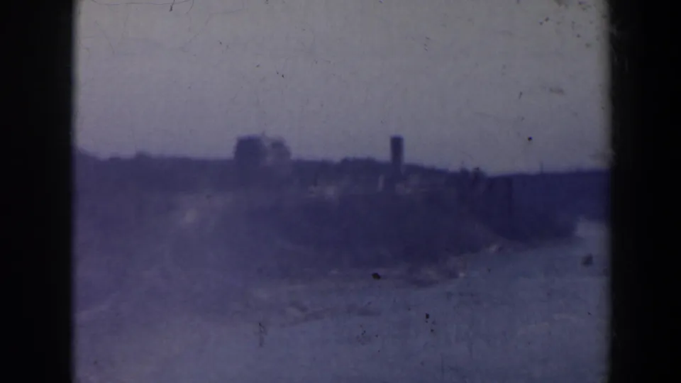 1963 8mm Niagara Falls area view with distant buildings, a tower-like form, haze, grain and dark frame-edge shadows.