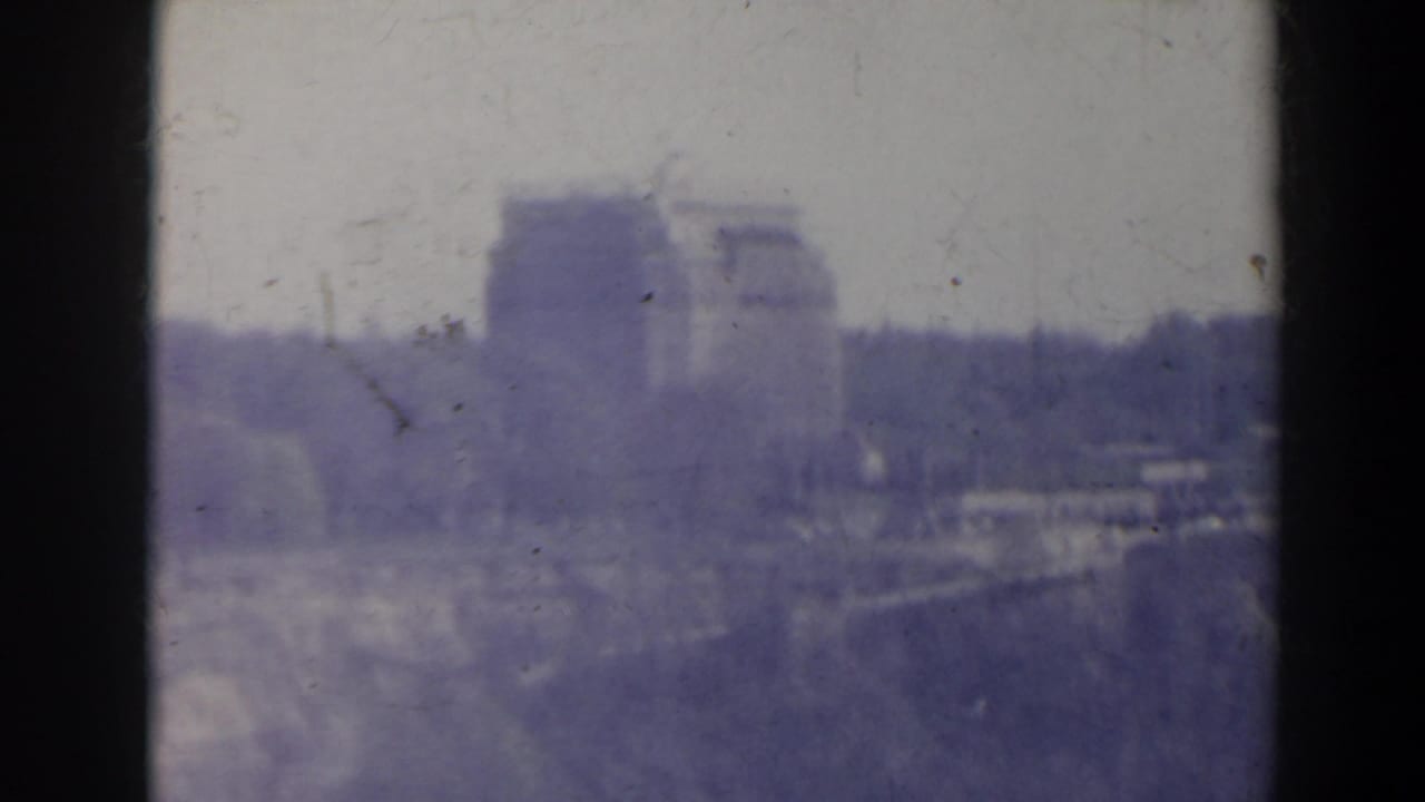 Large distant building complex seen through haze with trees and a pale sky.