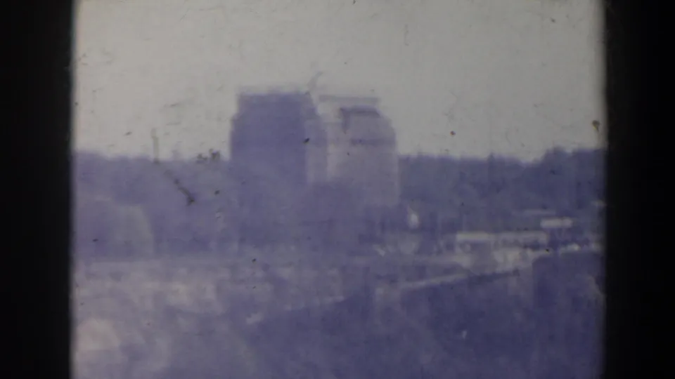 Hazy 1963 8mm view near Niagara Falls, Canada, showing a large distant building complex above a tree line.