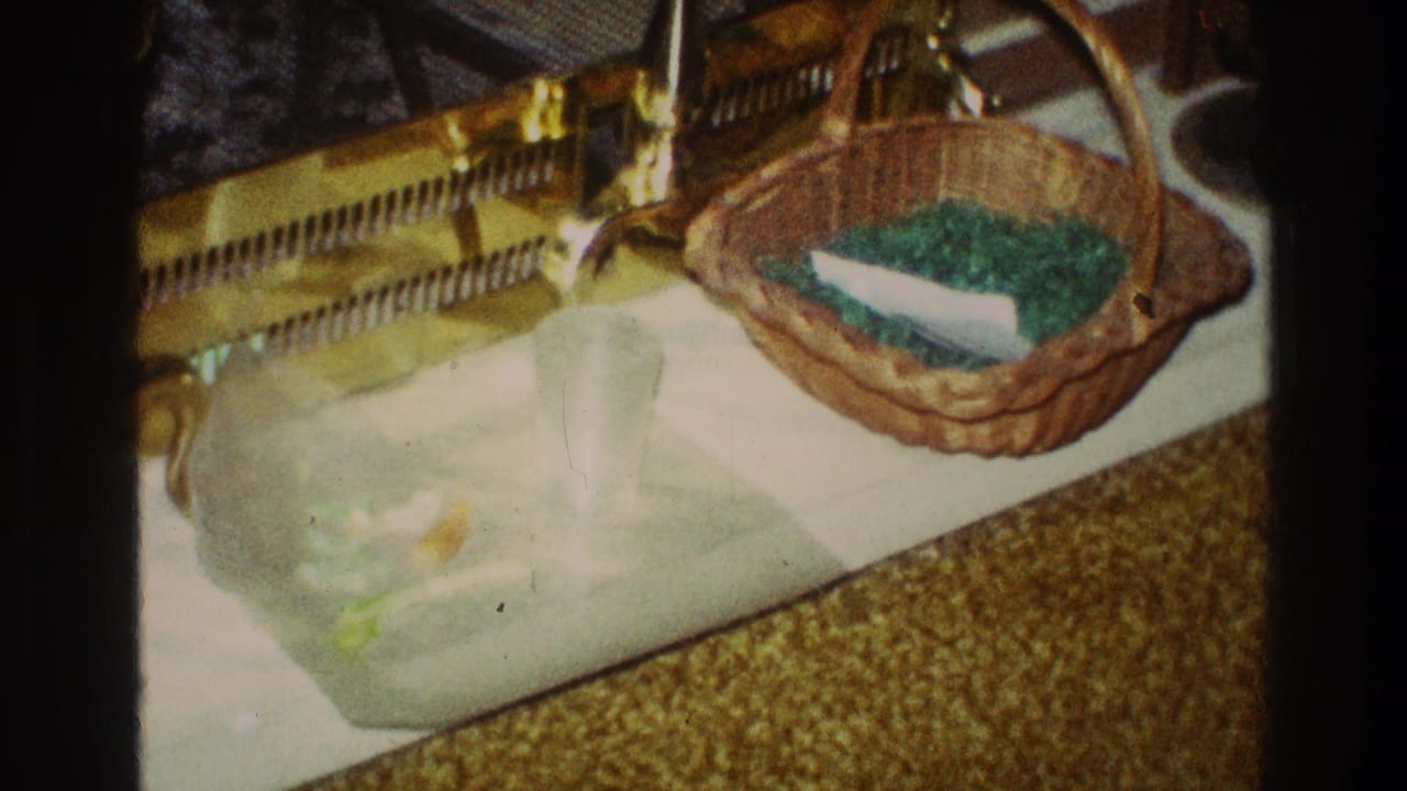 A private interior frame from the 1969 Clarendon Hills 8mm clip shows an Easter basket with green grass resting on a white tray near a brass fireplace tool set.