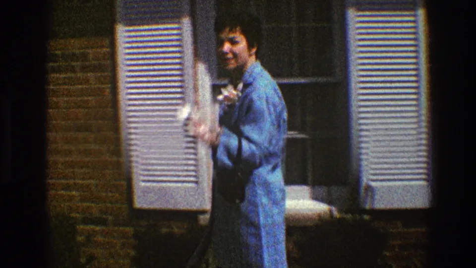 The woman turns toward the camera near a shuttered window on a brick house exterior in Clarendon Hills, Illinois.