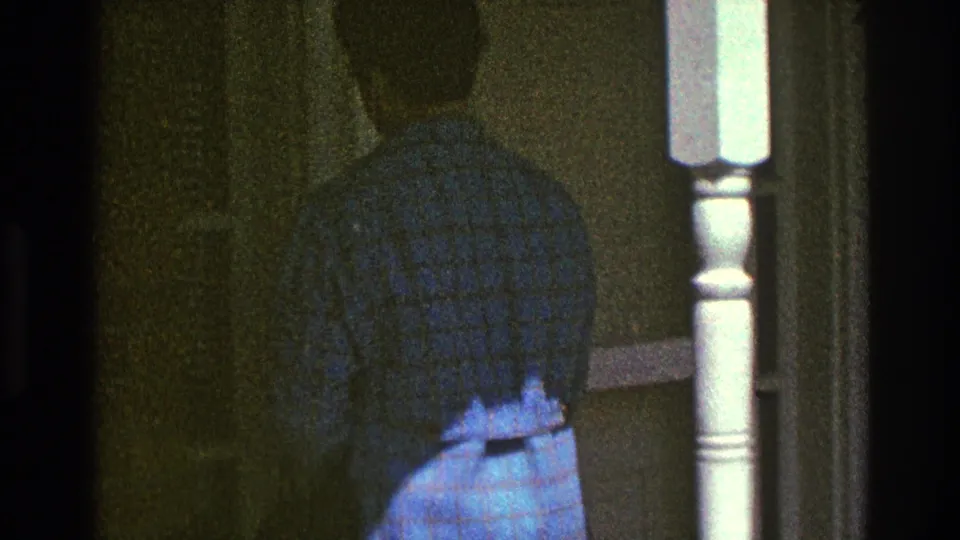 The woman is seen from behind in her blue plaid coat as she moves toward a doorway beside a light porch column.