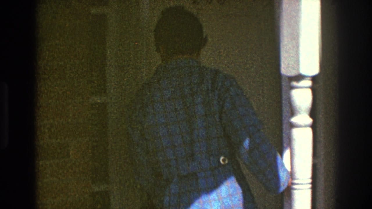 In Clarendon Hills, Illinois, 1969, a man in a blue checkered jacket and hat moves toward a residential door beside a white porch post.