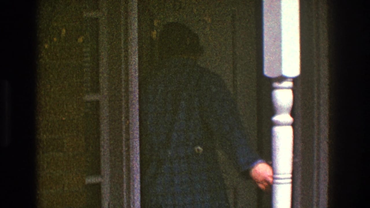The man in the blue checkered jacket reaches the doorway of the Clarendon Hills house, partly obscured by the porch post and film shadow.