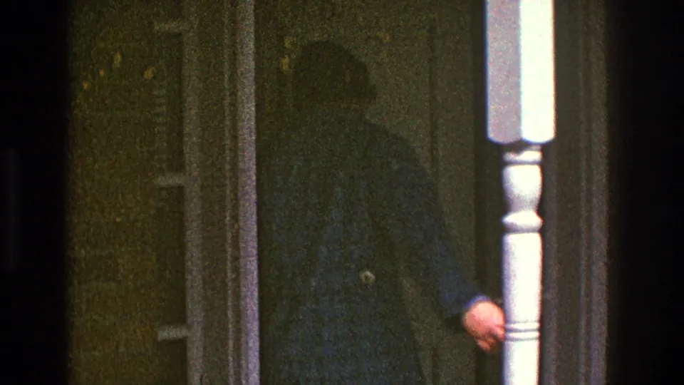 The man in the blue checkered jacket reaches the doorway of the Clarendon Hills house, partly obscured by the porch post and film shadow.
