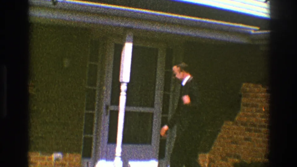 The suited man turns from the camera toward the doorway of a brick home in Clarendon Hills, Illinois, in 1969.