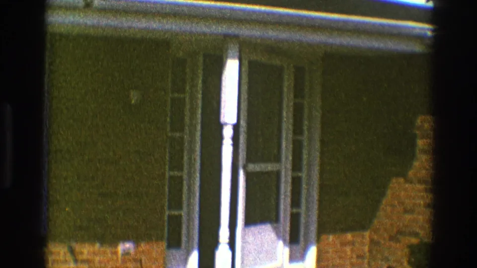 1969 Clarendon Hills 8mm frame showing a white-framed front entrance with glass panels, sidelights, dark wall, brick base, and film edge vignette.